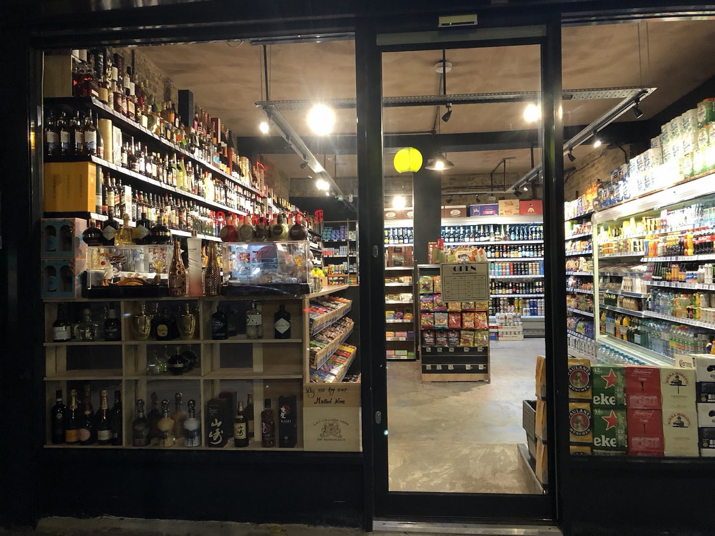 Inside Vintage Bottle at night, the wine wall on one side and chilled beer and grocery aisles on the other