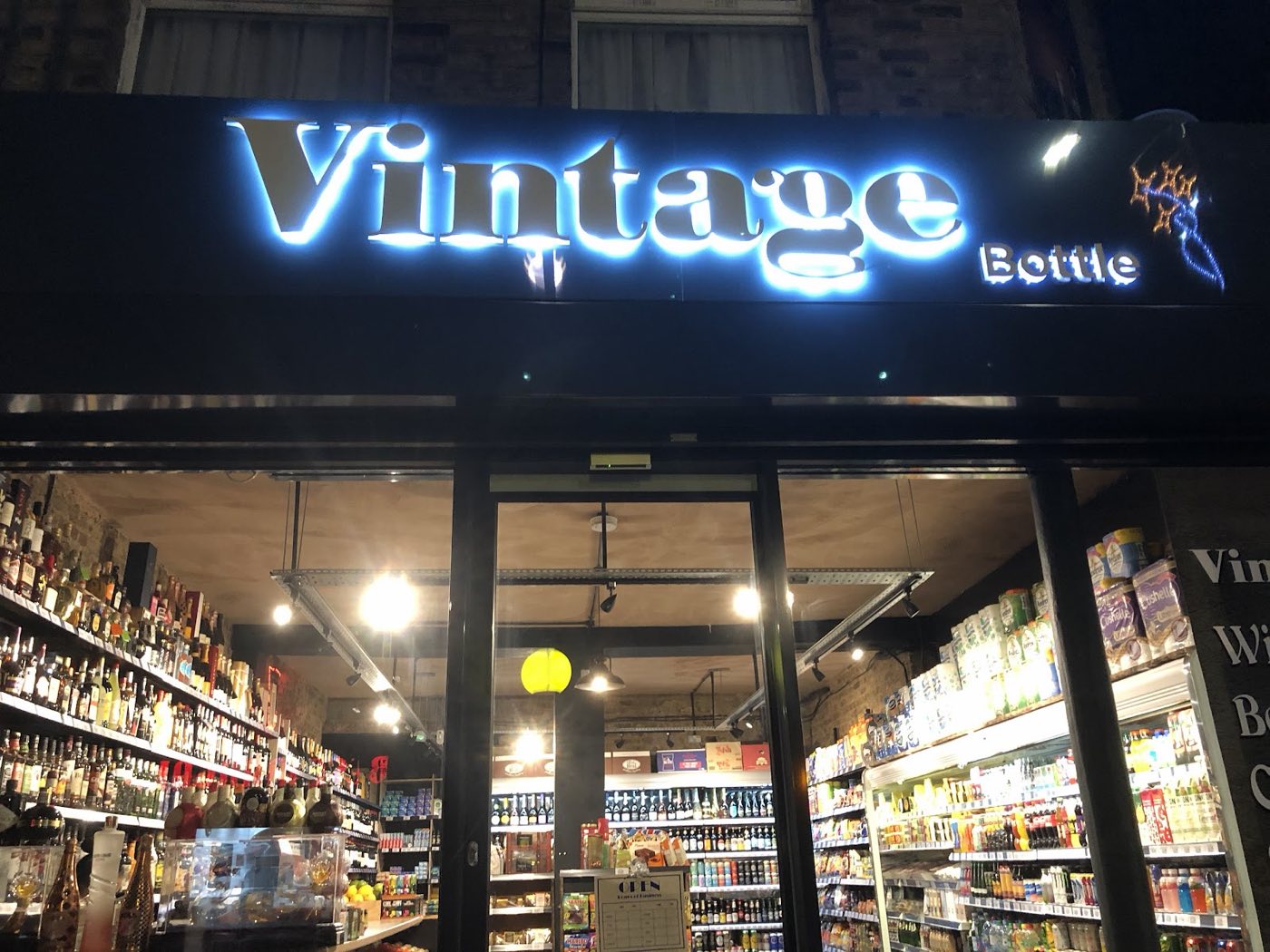 The illuminated Vintage Bottle shopfront sign lit up at night on Chatsworth Road